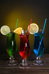 Glasses of cocktails on table on dark yellow background