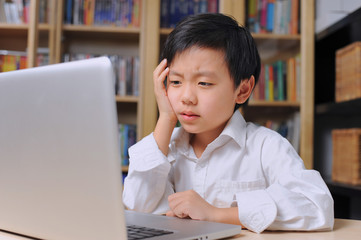 Asian boy thinking hard in front of laptop computer