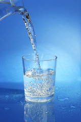 Pour water from  pitcher into  glass, on dark blue background