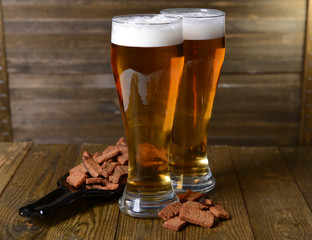 Glasses of beer with snack on table on wooden background