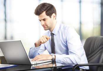 Fototapeta premium Happy young businessman using laptop in his office