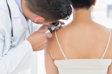Dermatologist examining mole on back of woman