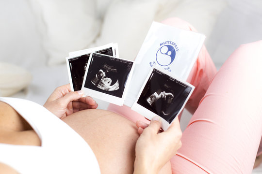 Schwangere Frau liegend hält Ultraschallbilder und Mutterpass