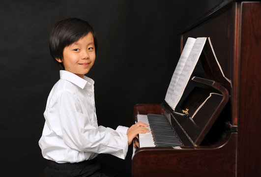 Young Asian Boy Playing Piano (isolated On Black Background)