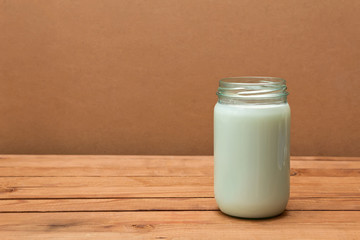 Open glass jar with fresh milk on a wooden table
