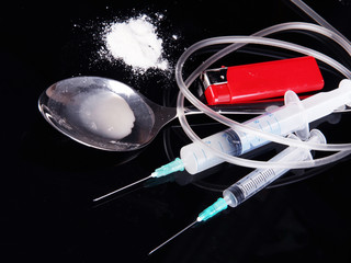 Heroin in spoon and syringes on black background