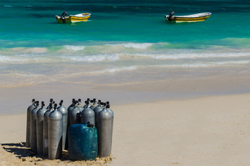Scuba diving air tanks on sandy Caribbean beach with boats - obrazy, fototapety, plakaty