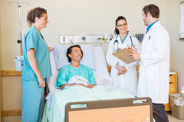 Doctors Discussing Report While Nurse And Patient Looking At The