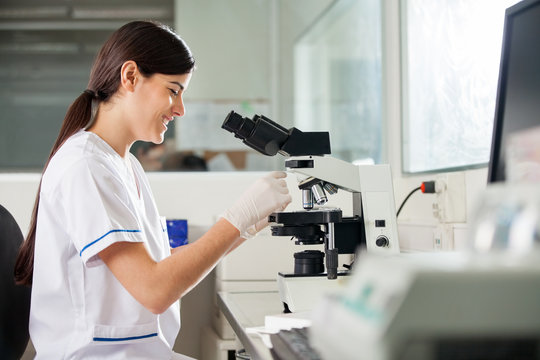 Happy Female Scientist Using Microscope In Lab