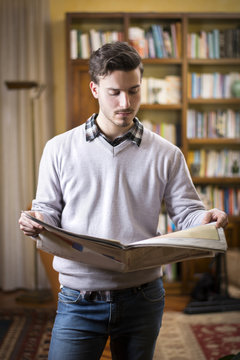 Handsome young man reading newspaper at home