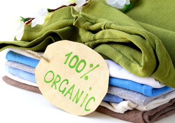 stack of multicolored clothing with 100% organic label - obrazy, fototapety, plakaty