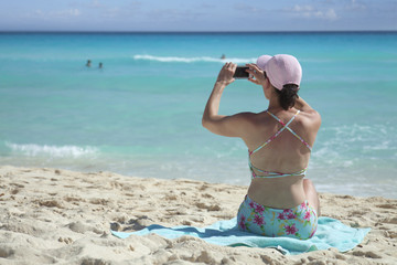 Beautiful woman takes smartphone pictures at the beach