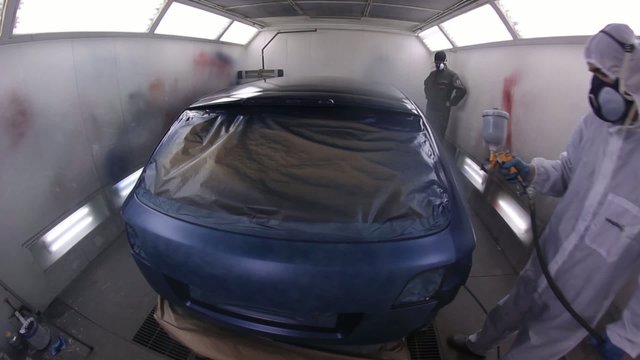 A man varnishing a blue car in a painting chamber...