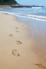 Human footprints on the beach sand leading towards the viewer