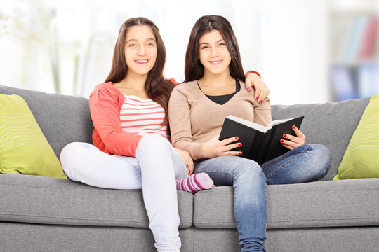 Two teenage girls posing seated on couch, indoors