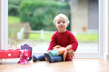 Lovely little blonde toddler girl playing with doll