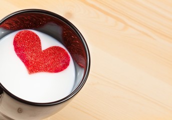 cup of milk with decorative heart on wood table