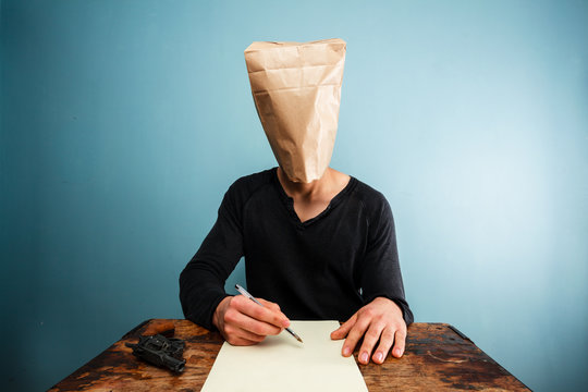 Man with bag over head writing suicide note