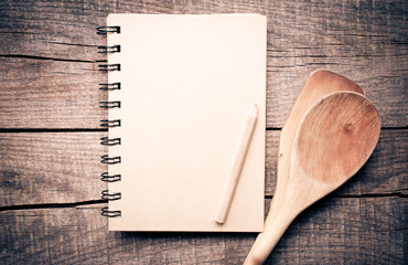Old recipe notebook, spoons on wood background 