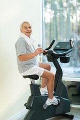 Senior man with bottle of water on a bike in a fitness club