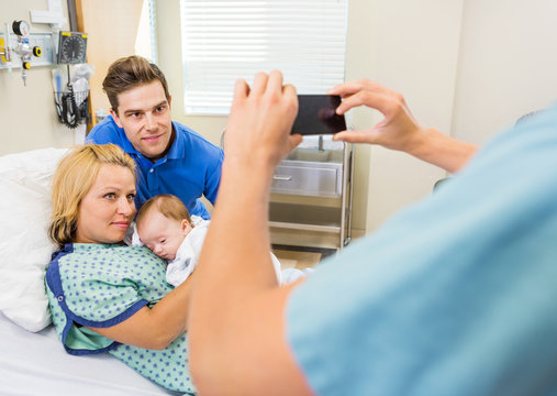 Nurse Photographing Couple With Newborn Baby Through Mobilephone