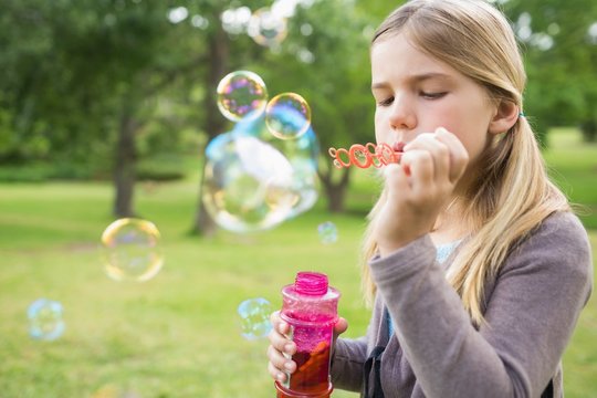 Girl blowing soap bubbles at park