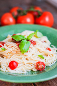 Spaghetti with tomatoes and basil on wooden background