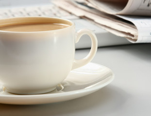 cup of coffee near the laptop and newspapers.