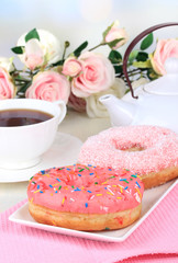 Sweet donuts with cup of tea on table on light background