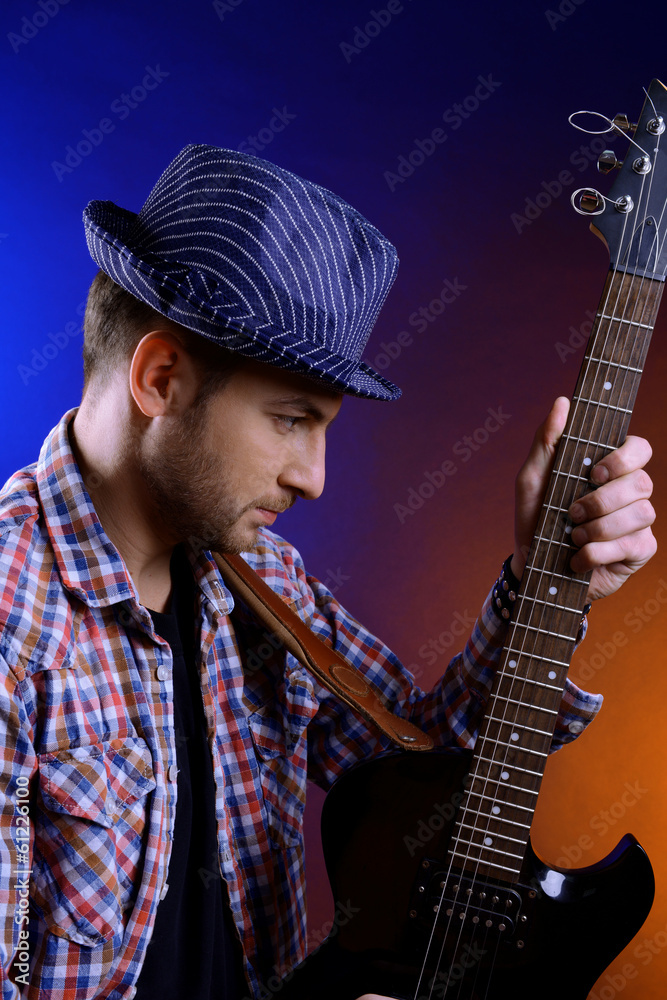 Poster Young musician playing  guitar on dark color background