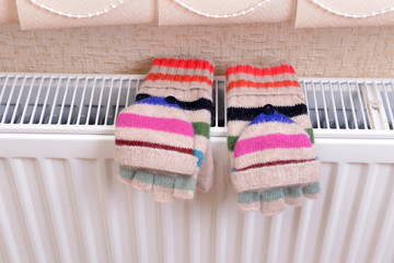 Obraz na płótnie Canvas Knitted gloves drying on heating radiator