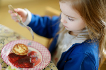 Cute little girl eating pancakes with jam