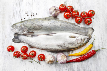 Two rainbow trouts, tomatoes and chili peppers on rustic wooden
