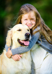 Little girl embraces her golden retriever in the summer park