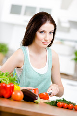 Girl slices vegetables for salad sitting at the kitchen 
