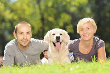 Smiling young couple lying on grass and hugging a dog in park