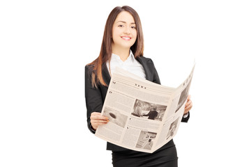 Young businesswoman in suit leaning on wall with a newspaper