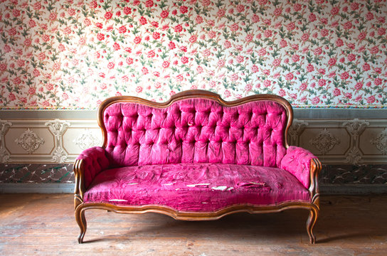 Old damaged red couch in an antique house. Flowers wallpaper