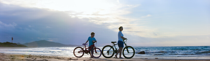 Mother and son biking at beach - obrazy, fototapety, plakaty