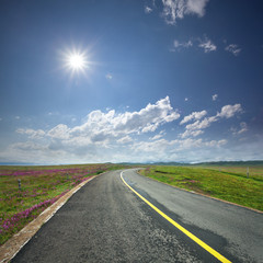 asphalt road through the green field and clouds on blue sky in s
