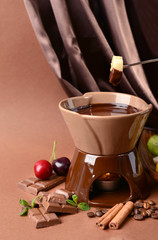 Chocolate fondue with fruits, on  brown background
