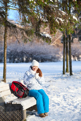 Fototapeta na wymiar Pretty woman with backpack sitting on a bench in winter park