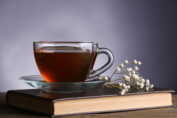 Cup of hot tea on book with flowers on table on gray background