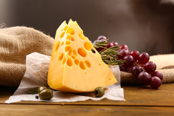 Piece of cheese on plate with green olives, on wooden