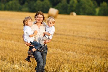 Young mother and two little twins boys having fun on yellow hay