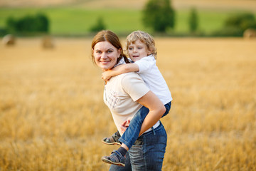 Young mother and her little son having fun on yellow hay field