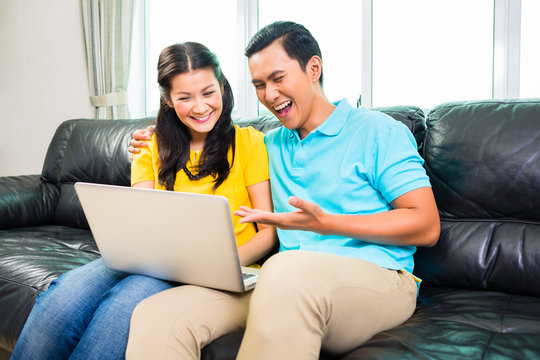 Asian Couple Using Laptop On Sofa