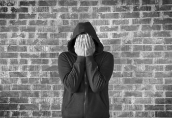 young man covers his face with hands with bricks wall