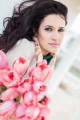 Beautiful young brunette woman with pink tulips in her hand