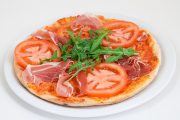 pizza with prosciutto, tomato and arugula on white plate